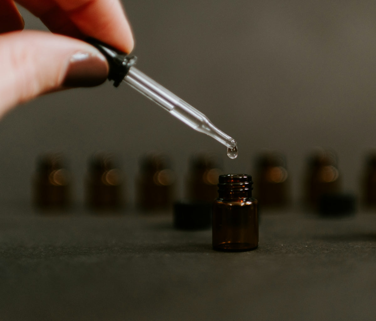 A single drop of oil falling from a glass dropper into an amber bottle