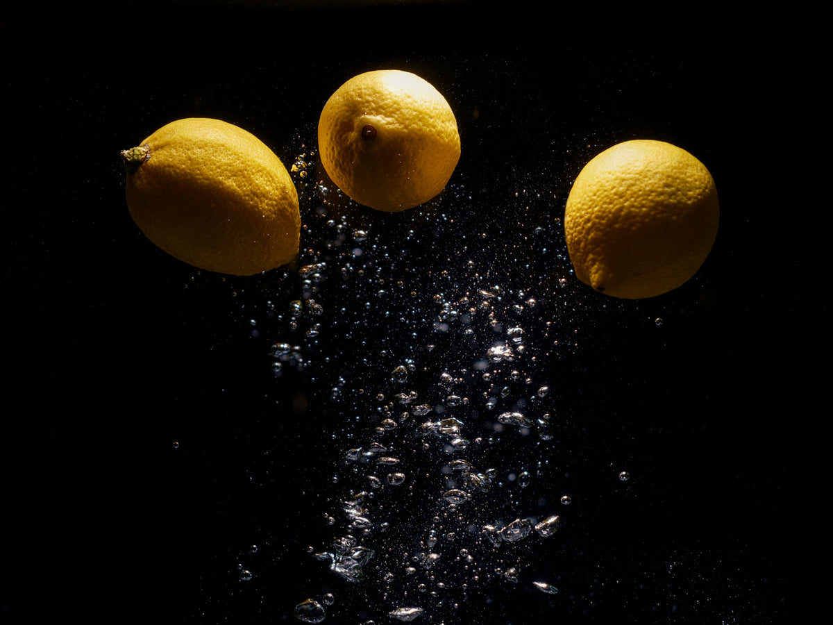 Three lemons splashing into water against a black background